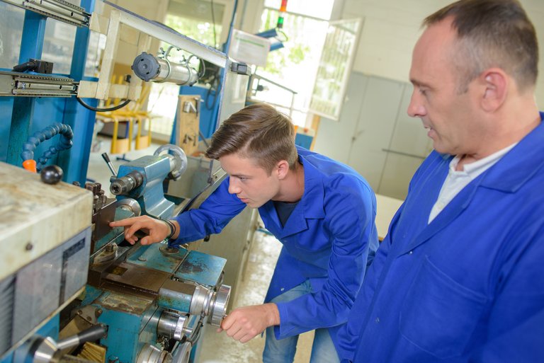 Ein Mann und ein Junge in Blaumann arbeiten an einem Werktisch
