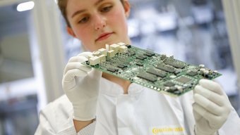 Das Bild zeigt eine Continental-Mitarbeiterin, die eine optische Überprüfung eines Karosseriesteuergeräts durchführt.