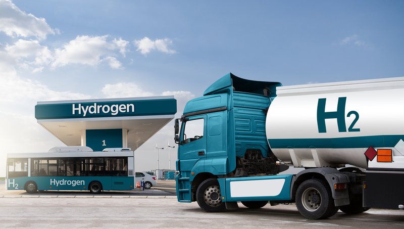 A semitrailer truck, a bus, and a car with turquoise paintwork at a hydrogen filling station
