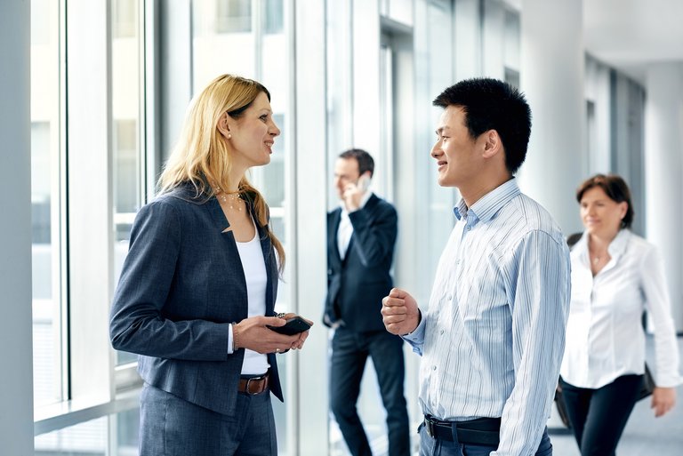 Two men and two women in business outfits walk down a hallway smiling