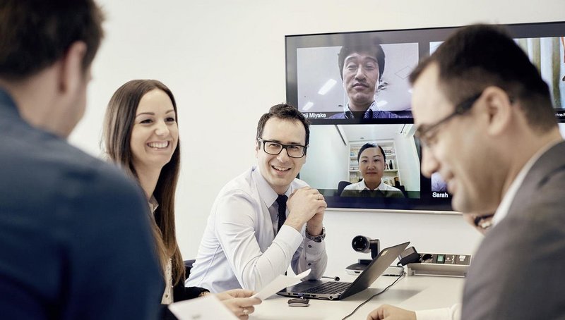 Four employees are having a meeting with international colleagues via video and telephone conference