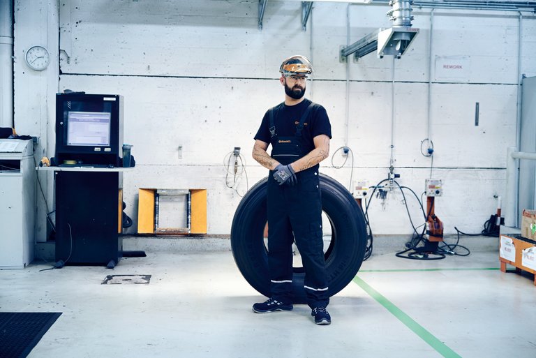 A man wearing safety goggles stands in front of a large tire in a testing hall