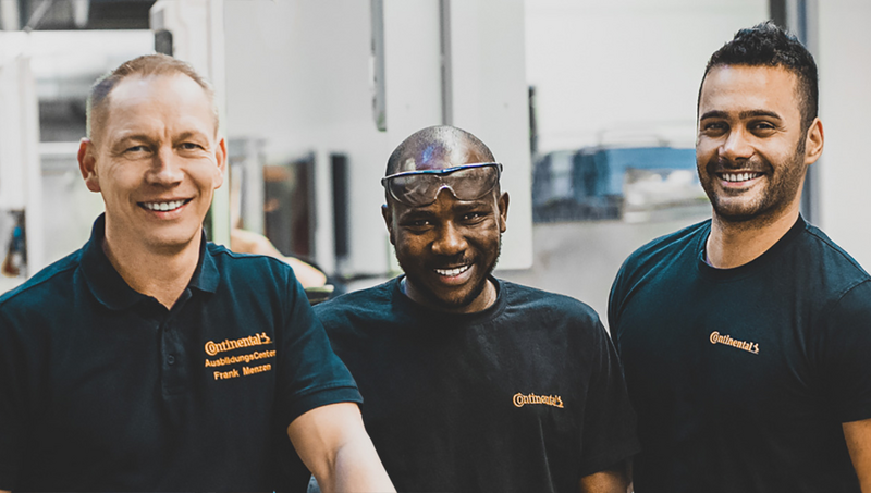 Three men in black Continental polo shirts standing in a factory and smiling