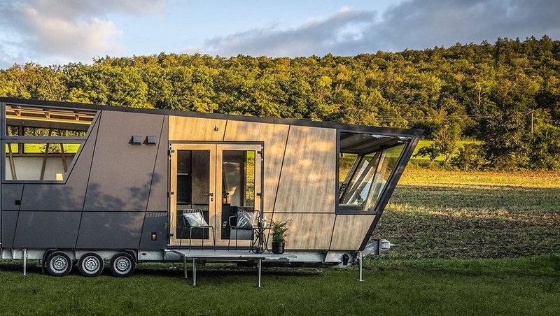 Ein futuristisches Tiny-House steht auf einer Wiese vor einer Waldböschung