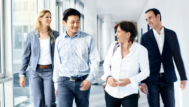 Two men and two women in business outfits walk smiling down a corridor