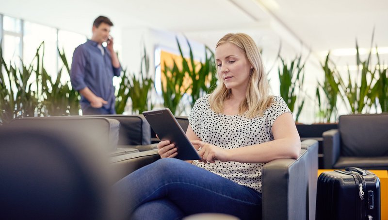 Eine Frau sitzt in einer Lounge und arbeitet mit einem Tablet