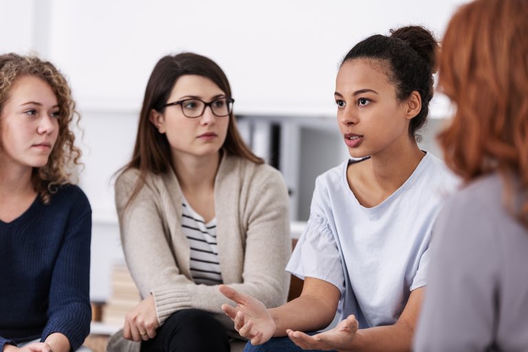 Vier junge Frauen sitzen im Kreis und schauen sich konzentriert an