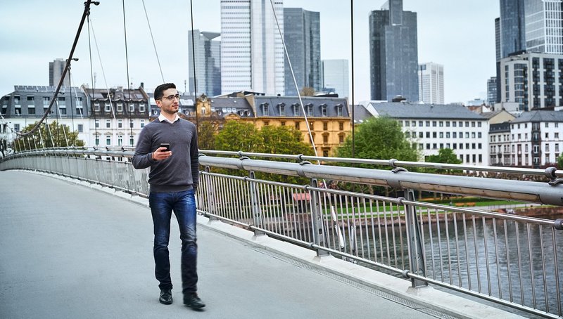 Ein junger Mann geht über eine Brücke vor der Skyline von Frankfurt