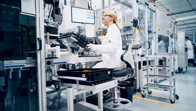 A young woman works in an ergonomic workspace where she can work both sitting and standing and is supported by machines